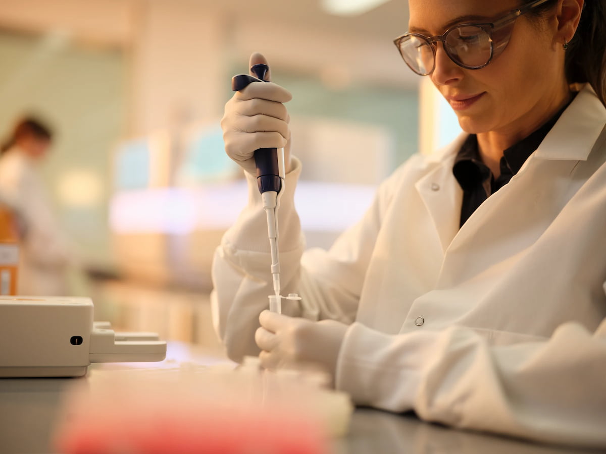 Close up image of a female scientist pipetting clear liquid into tube; NextSeq 1000/2000 reagent cartridge and box in the background.
